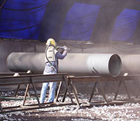 Man using automatic sprayer to paint a large cement pipe gray