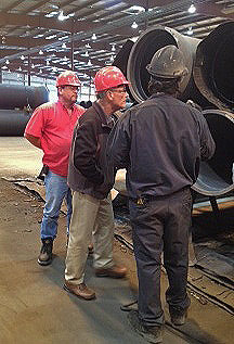 Three men in hardhats inspecting industrial pipes.