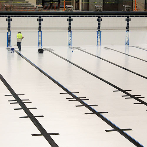 Man in yellow high visibility vest painting the bottom of an empty olympic sized swimming pool